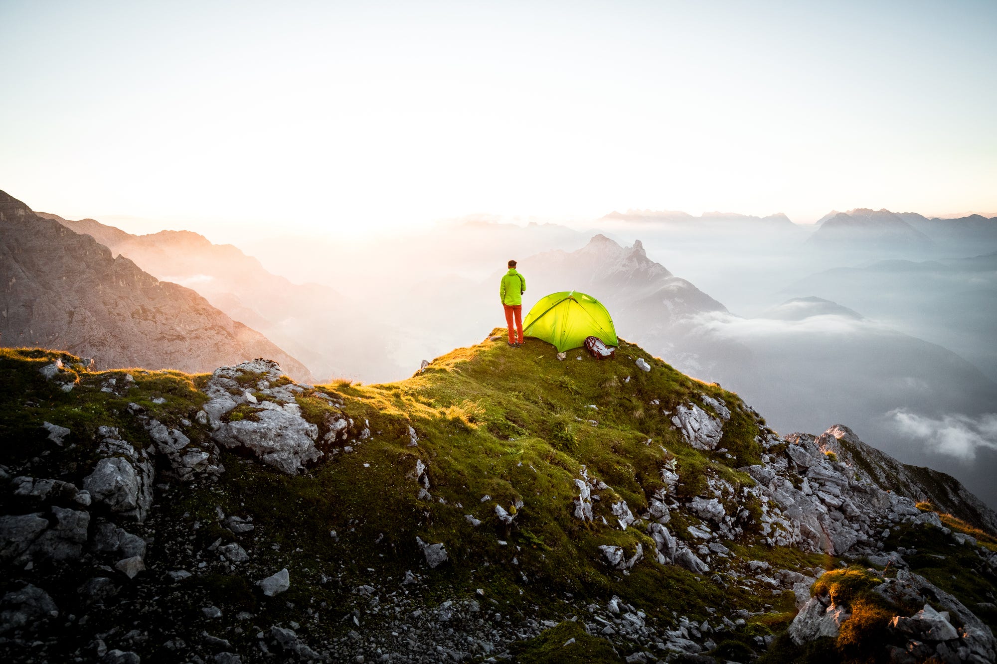 Man stands on mountain beneath tent