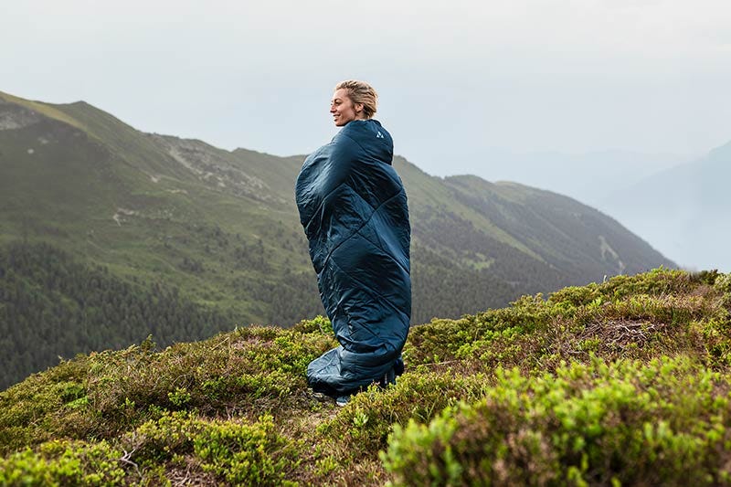 women in sleeping bag standing in front of mountains